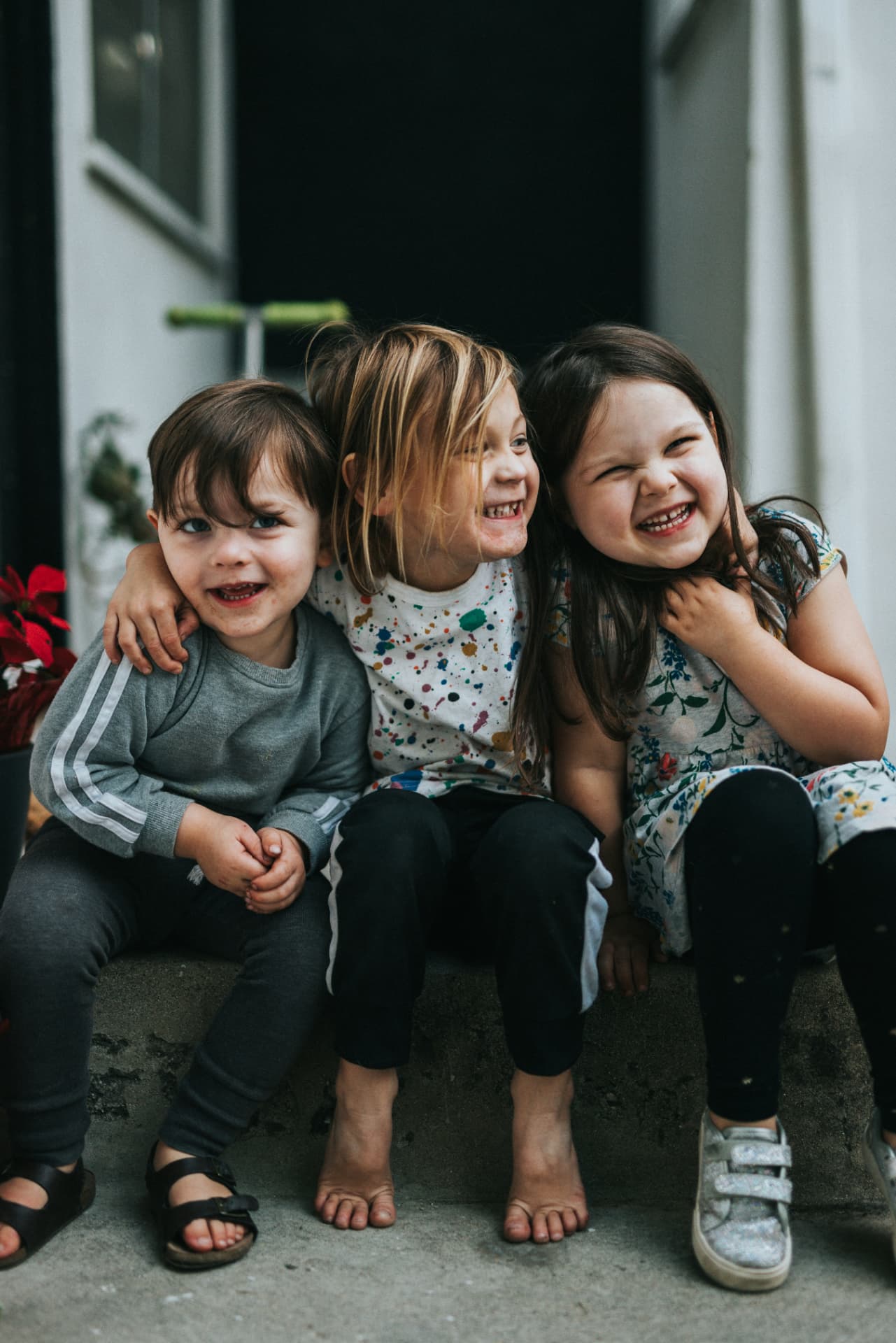 Three young children sitting together on a doorstep, arms around each other, laughing